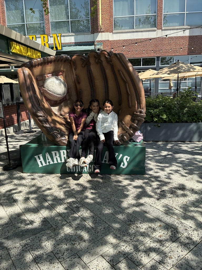 Three smiling individuals sit on a giant baseball glove sculpture at Harry Caray's in Chicago. The scene is cheerful, with sunny weather and outdoor seating.