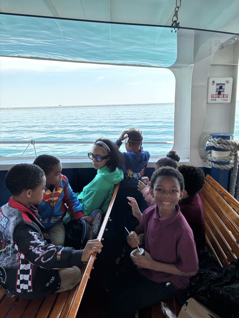 A group of smiling children sits on a boat, enjoying a sunny day on the water. The mood is joyful and relaxed, with clear skies visible outside.