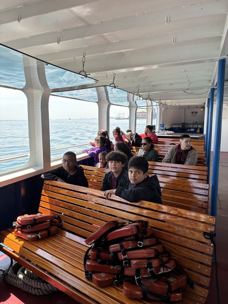 People sit on wooden benches inside a boat, gazing out at the ocean through large windows. A stack of red life jackets rests on a bench. The mood is relaxed.
