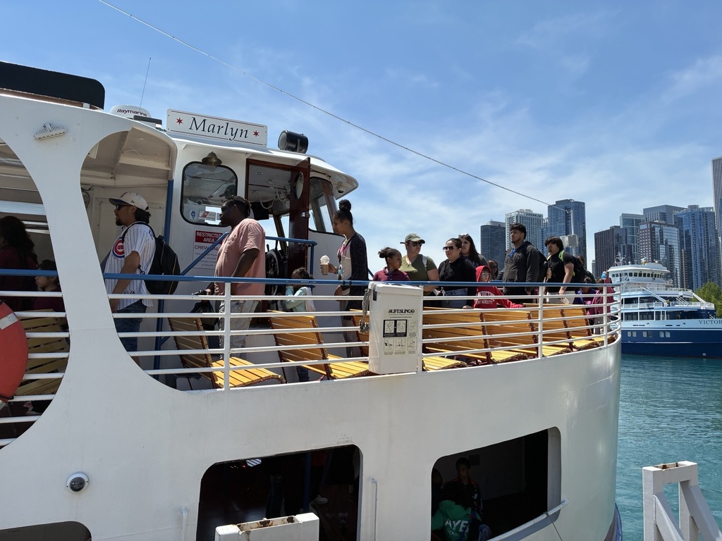 People boarding a white tour boat named "Marlyn" on a sunny day, with the Chicago skyline in the background. The mood is lively and anticipatory.