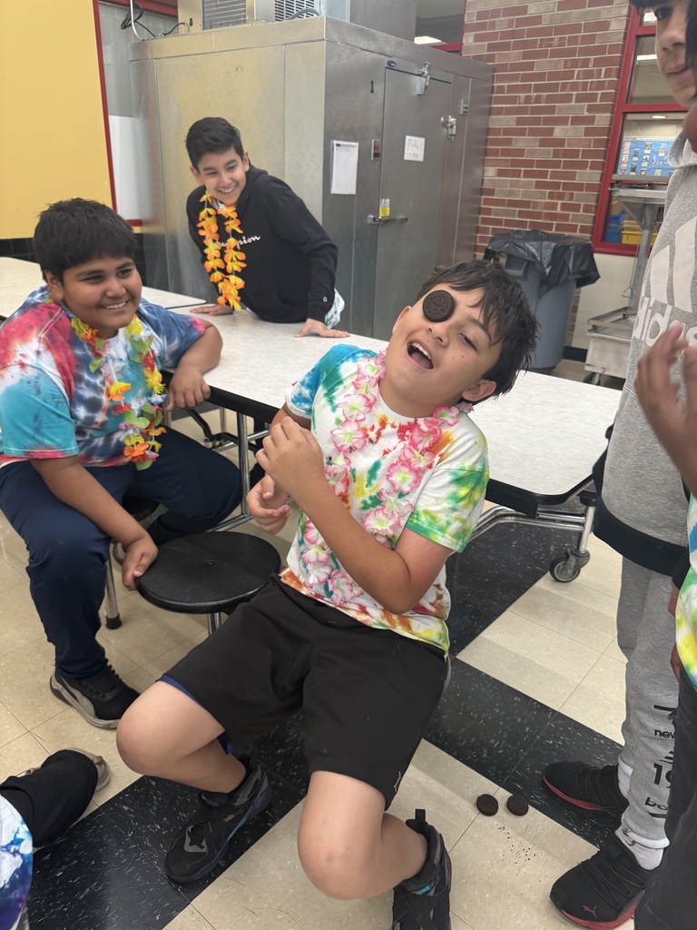 A joyful group of kids in a school setting, wearing colorful tie-dye shirts and flower leis. One child hilariously balances a cookie on his face.