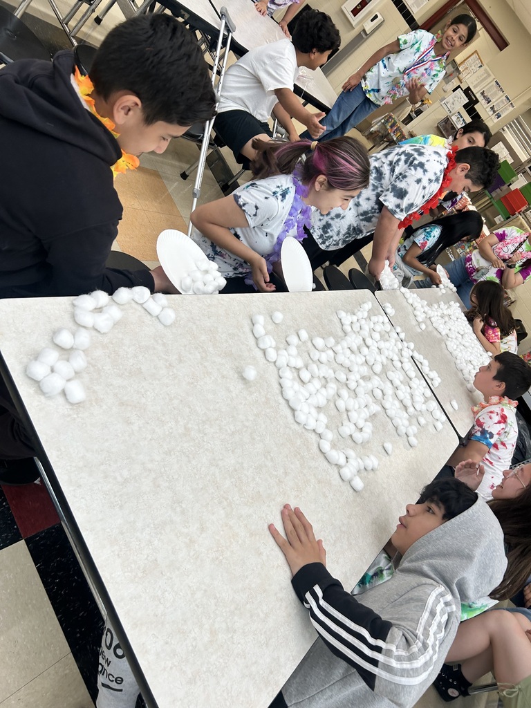 Children participate in a fun indoor activity at a cafeteria table, handling piles of cotton balls with excitement. The atmosphere is lively and engaging.