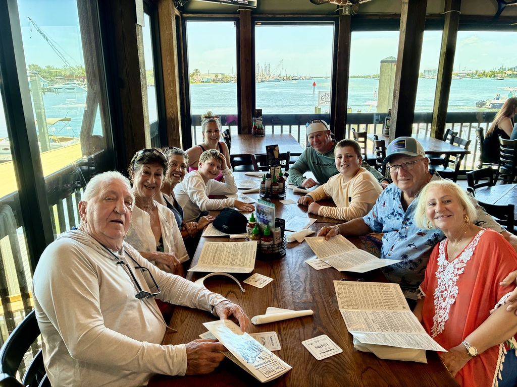 A group of nine people gathered around a table in a restaurant with menus smiling for a picture