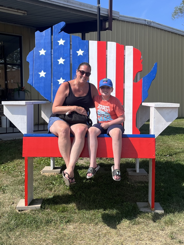 A woman and child sit on a bench resembling the United States, painted in American flag colors, smiling for a photo.