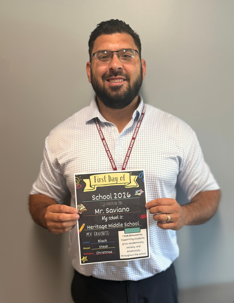 A man holding a sign that says "First Day of School 2026," featuring details about his role as a principal and his school.