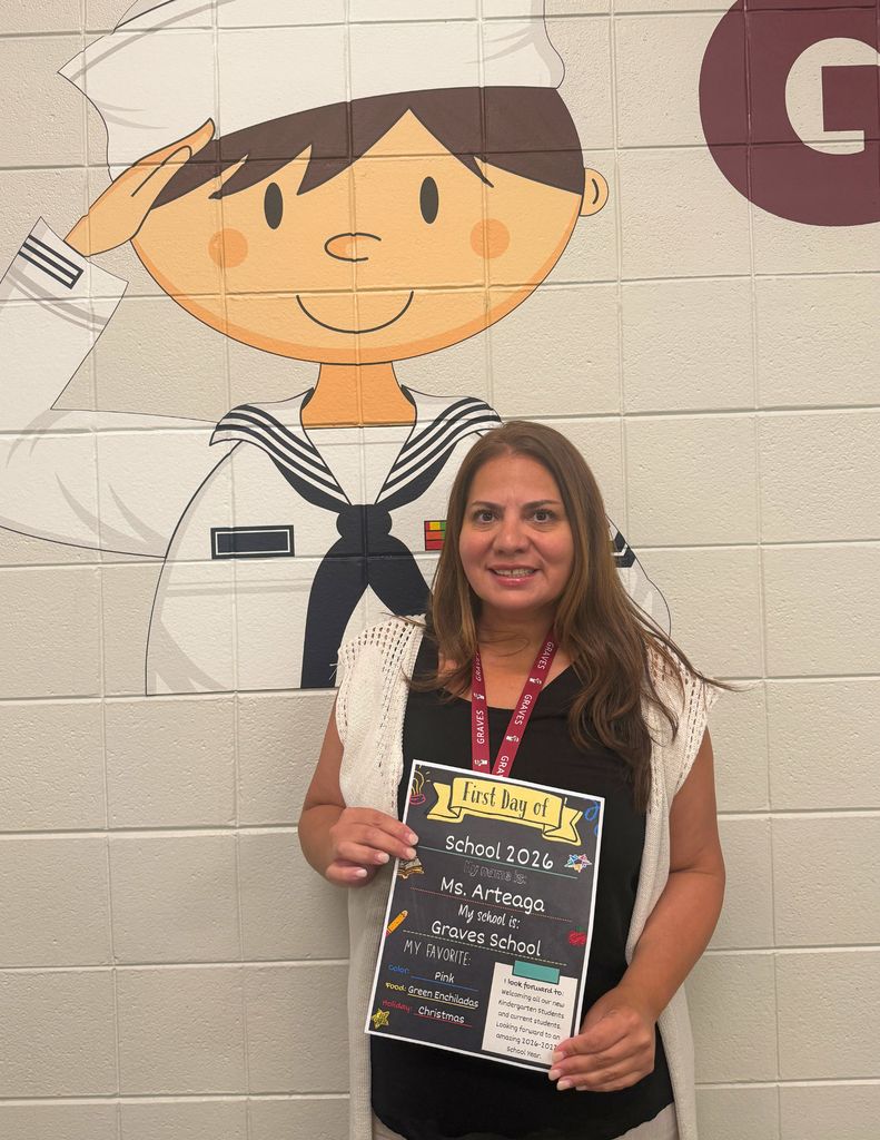 A woman holding a "First Day of School" sign stands in front of a mural depicting a sailor saluting.