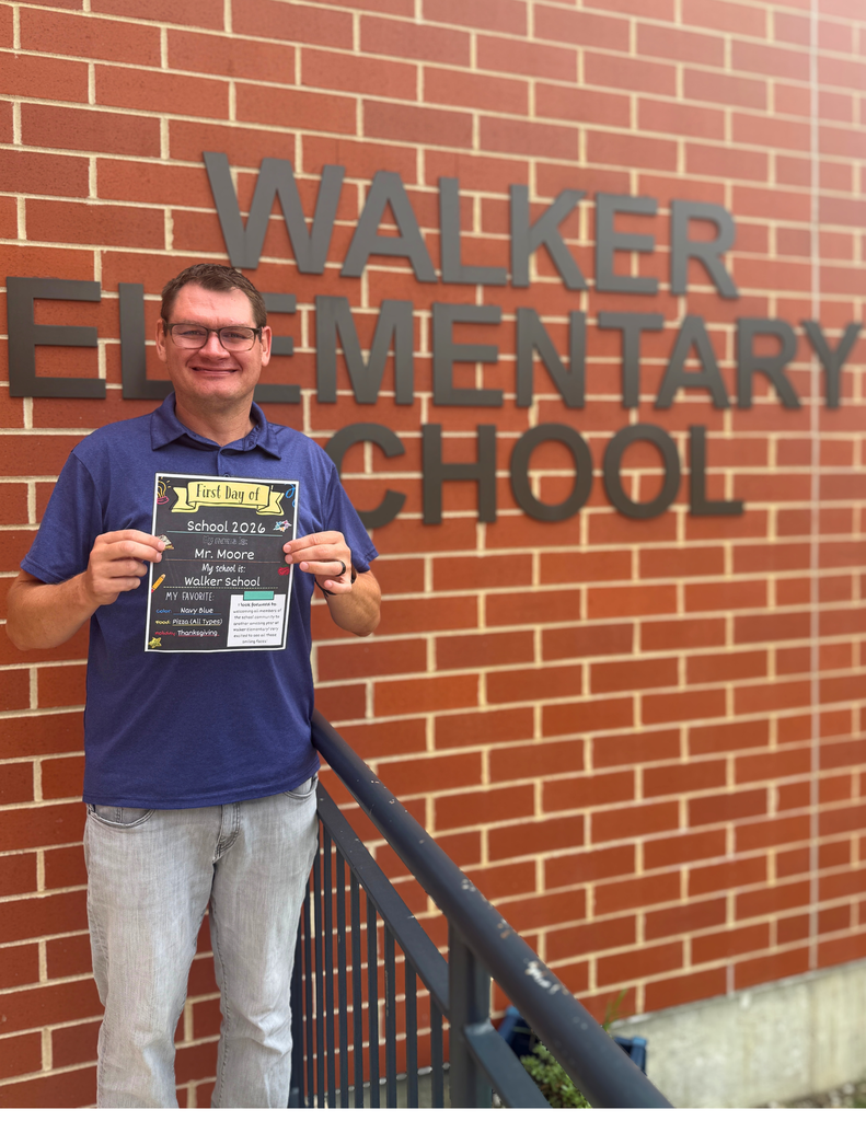 A man holding a certificate stands in front of a brick wall with the text "WALKER ELEMENTARY SCHOOL."