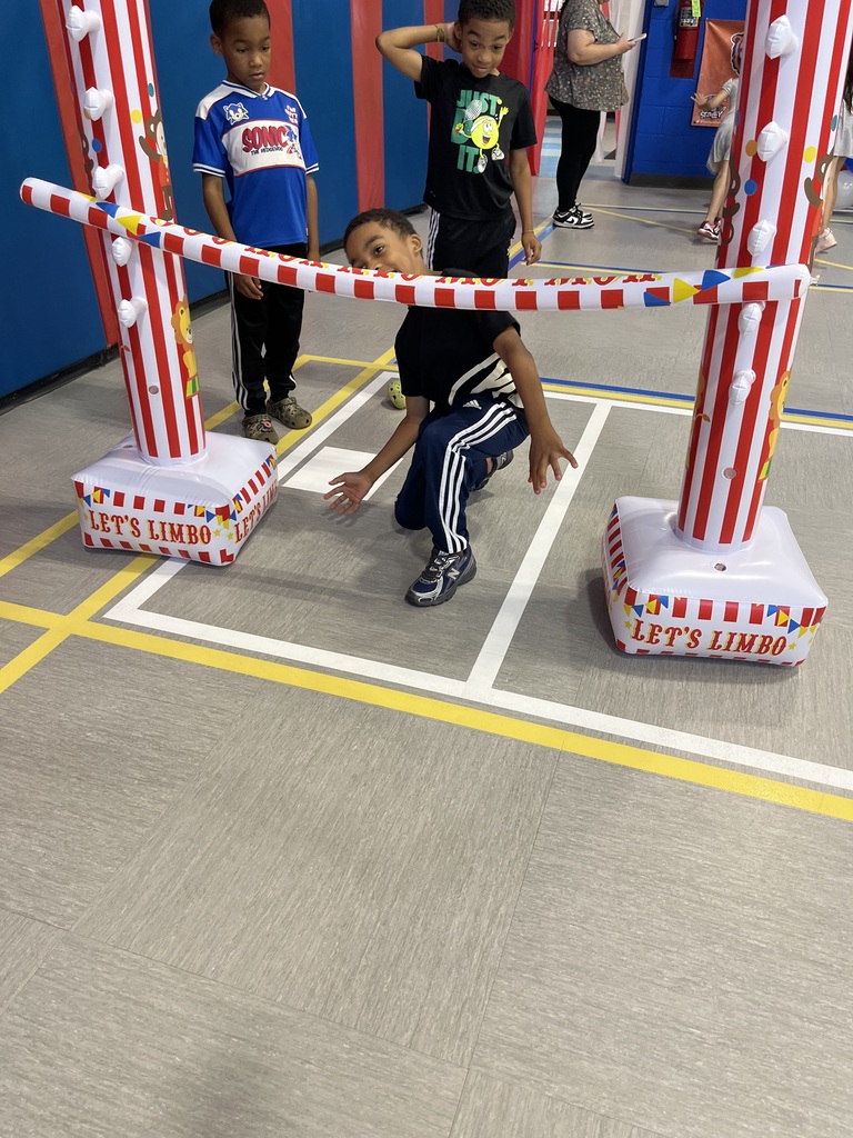 Children play limbo at a colorful striped bar labeled “Let’s Limbo,” as one child leans backward beneath it while others watch.