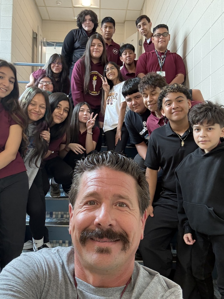 Smiling teacher takes a selfie with a diverse group of cheerful students gathered on a school staircase, creating a warm, celebratory mood.