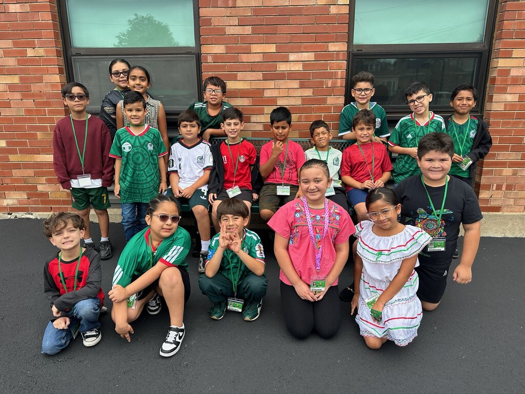 A cheerful group of children poses outside a brick building, wearing colorful shirts and lanyards, conveying friendship and teamwork.