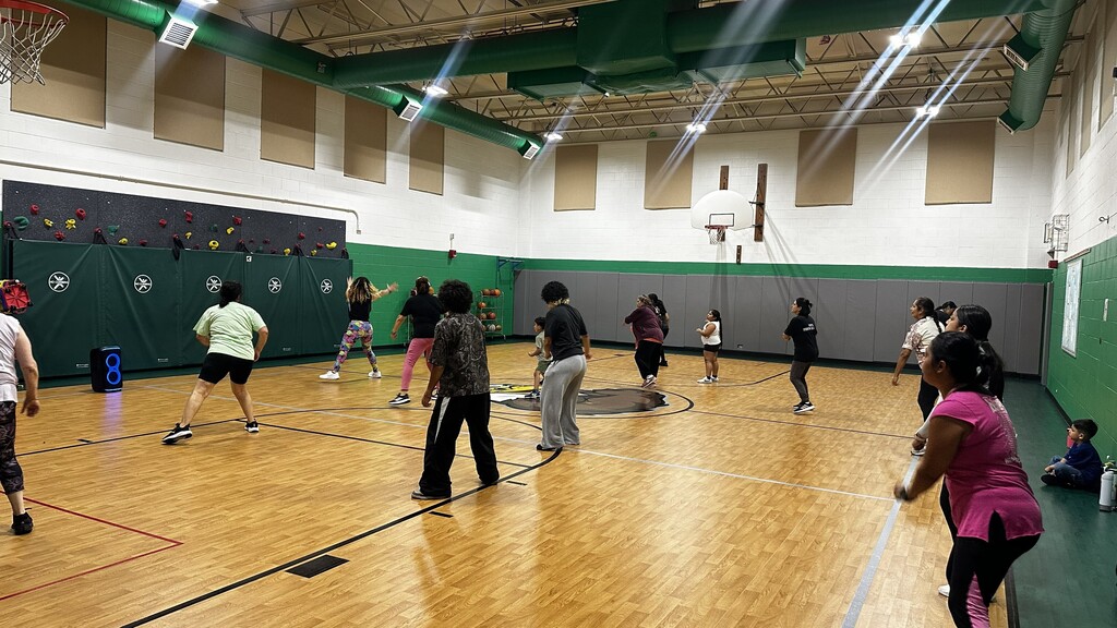 Adults play basketball in a bright indoor gym, dribbling and defending on a polished court; the energetic scene shows teamwork and fitness.