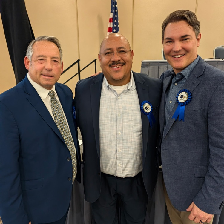 three men in suits posing for a photo at a conference center 