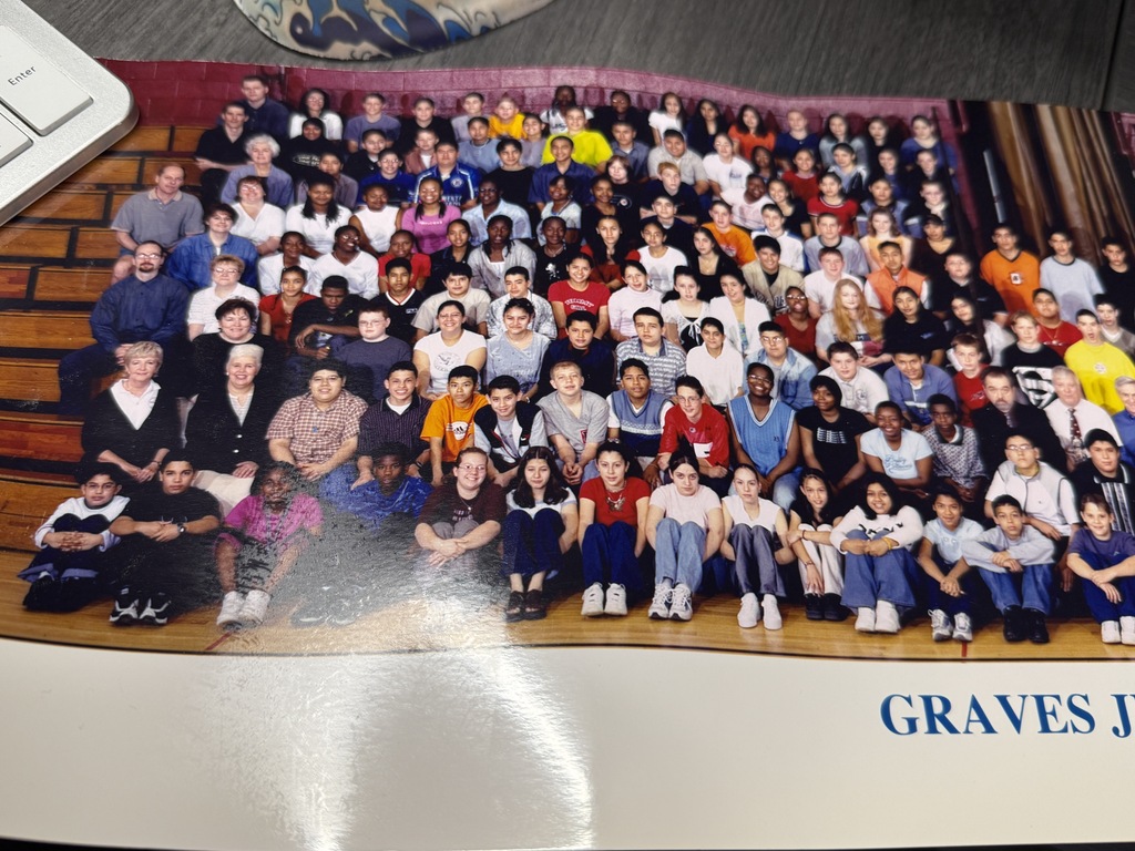 A large, diverse group of adults and young people pose in rows, many smiling, in a printed group photo with “GRAVES J...” visible below.