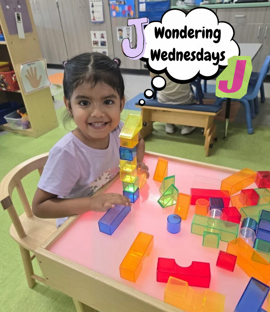 A smiling child stacks colorful translucent blocks at a classroom table, beneath a “Wondering Wednesdays” graphic featuring the letter J.