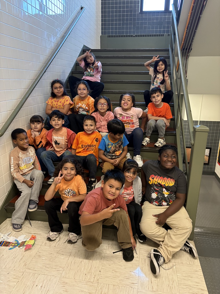 A cheerful group of diverse elementary-age children pose on school stairs, smiling and flashing peace signs in a bright hallway.