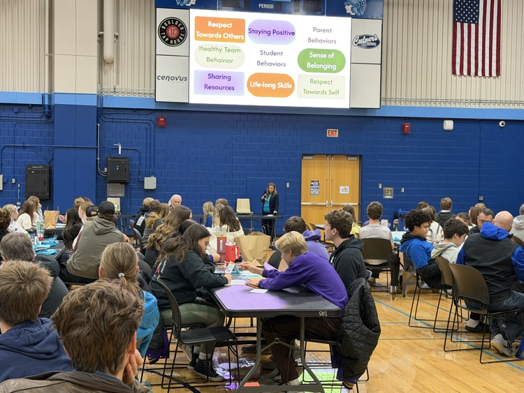 student groups from different school districts sitting in the large group session discussing sportsmanship topics they might consider that are listed on a large screen.  