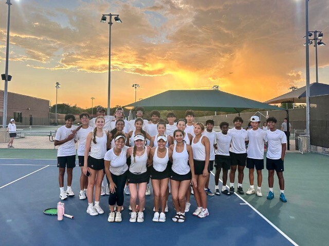 Photo of Coppell Tennis Team with white shirts and black shorts on a tennis court.