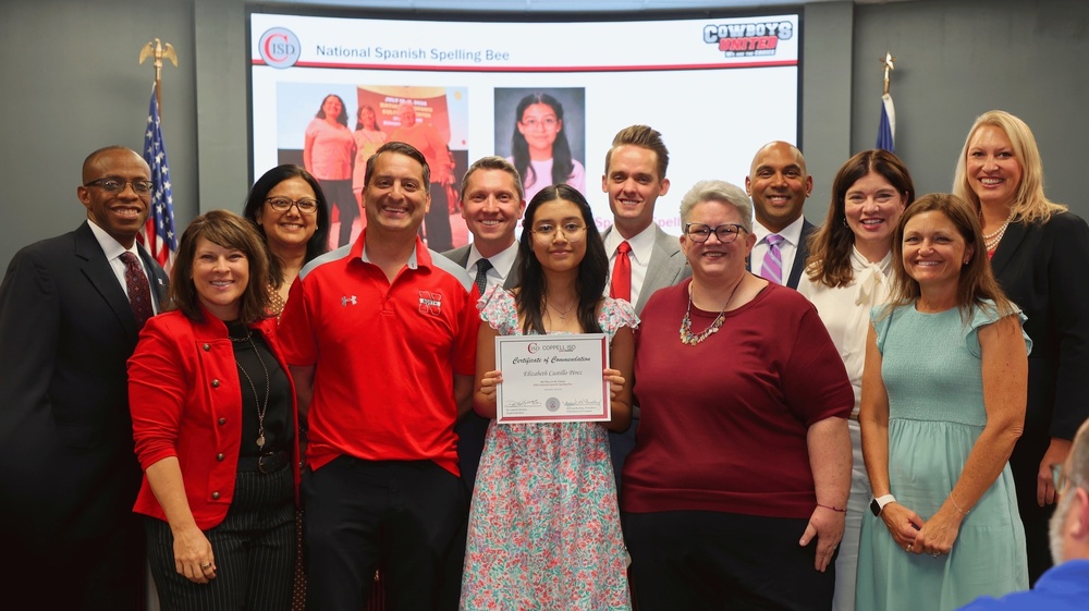 lizabeth Castillo Pérez, center, holds a Coppell ISD Certificate of Commendation while posing with CISD Trustees, Superintendent Dr. Leanne Shivers and staffin front of a presentation recognizing her participation in the National Spanish Spelling Bee.
