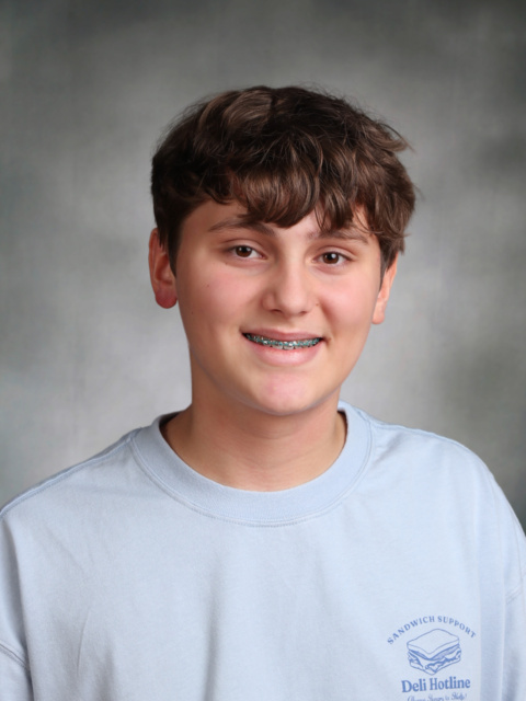 Asher Sharma smiles for a school portrait against a gray background, wearing a light blue shirt with a small Deli Hotline logo.