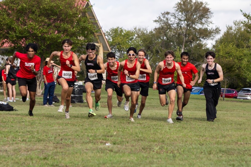 Cross Country Runners wearing red-and-black Coppell uniforms and race bibs compete across a grassy field.