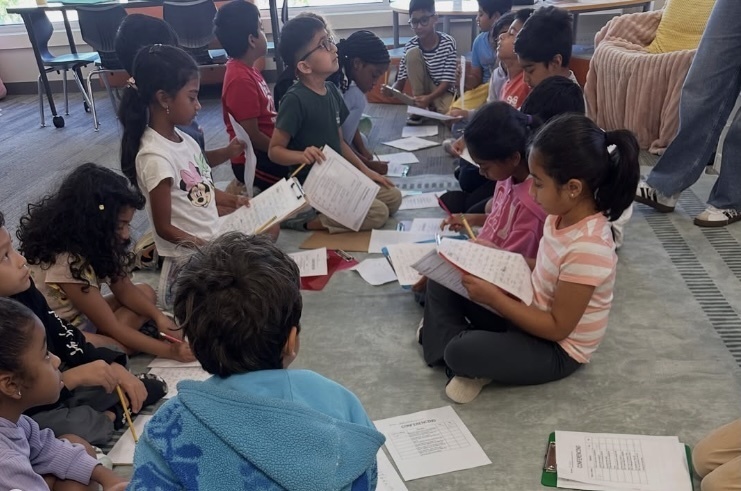 Canyon Ranch Elementary students sit in small groups on a classroom floor, writing on worksheets and discussing their work together.
