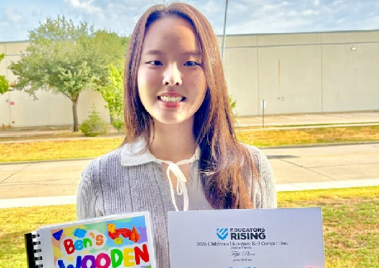 Yeseul Bak stands outdoors holding a colorful spiral-bound children’s book titled “Ben’s Wooden Blocks,” written and illustrated by Yeseul Bak, and a certificate from Educators Rising recognizing Yeseul Bak of Coppell High School, Texas, for fifth place in the 2026 Children’s Literature K-3 Competition, Junior Varsity, at the 2026 Educators Rising National Conference.