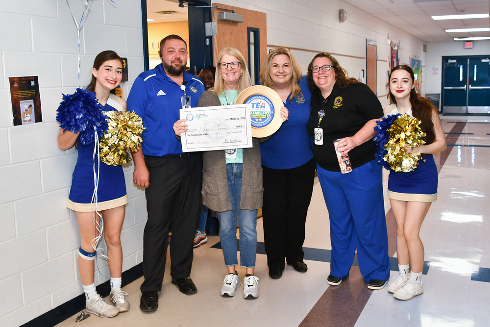 A group of people smiling in a school hallway holding awards