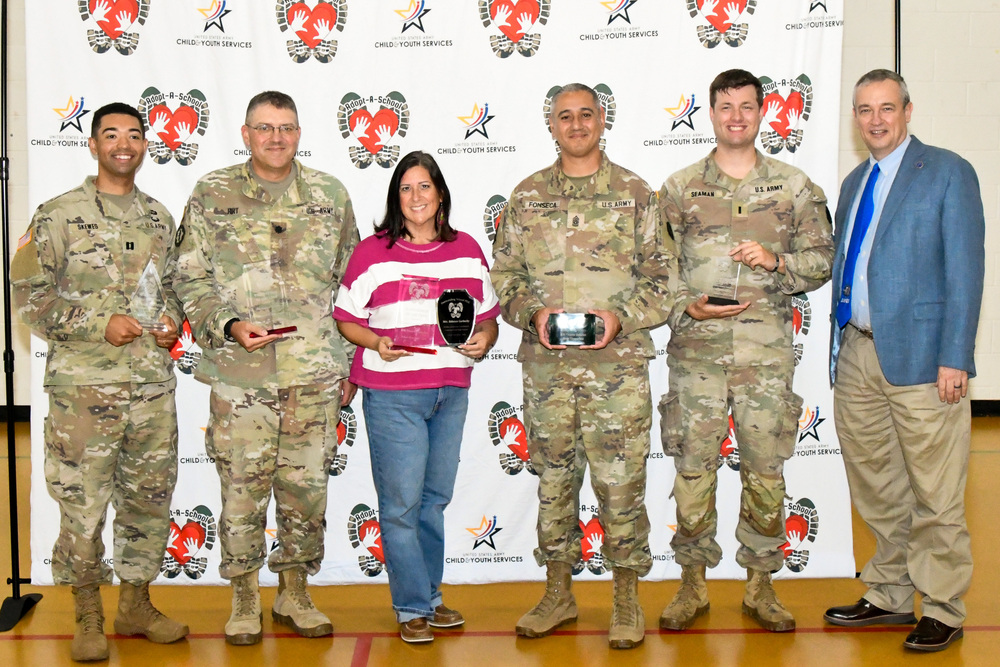 A man, woman and group of soldiers smiling and holding awards in front of a backdrop