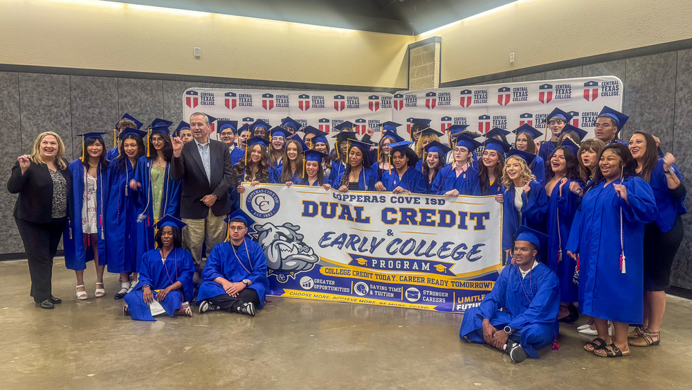 Students smiling in front of a backdrop with superintendents, holding a banner