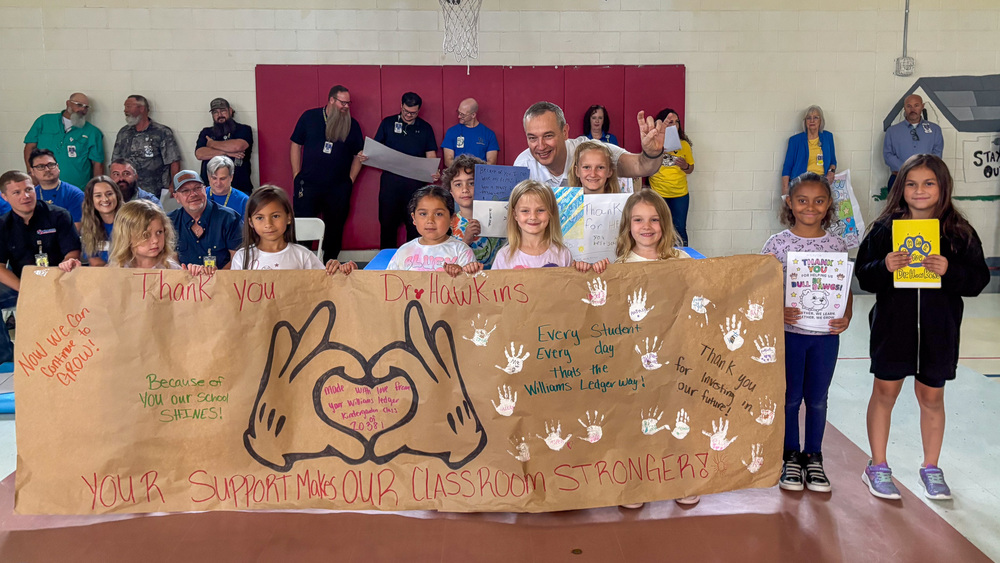 A group of students smiling and holding a banner with their superintendent.