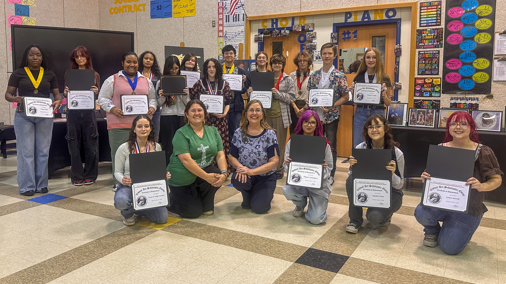 A group of students and two teachers smiling and holding awards