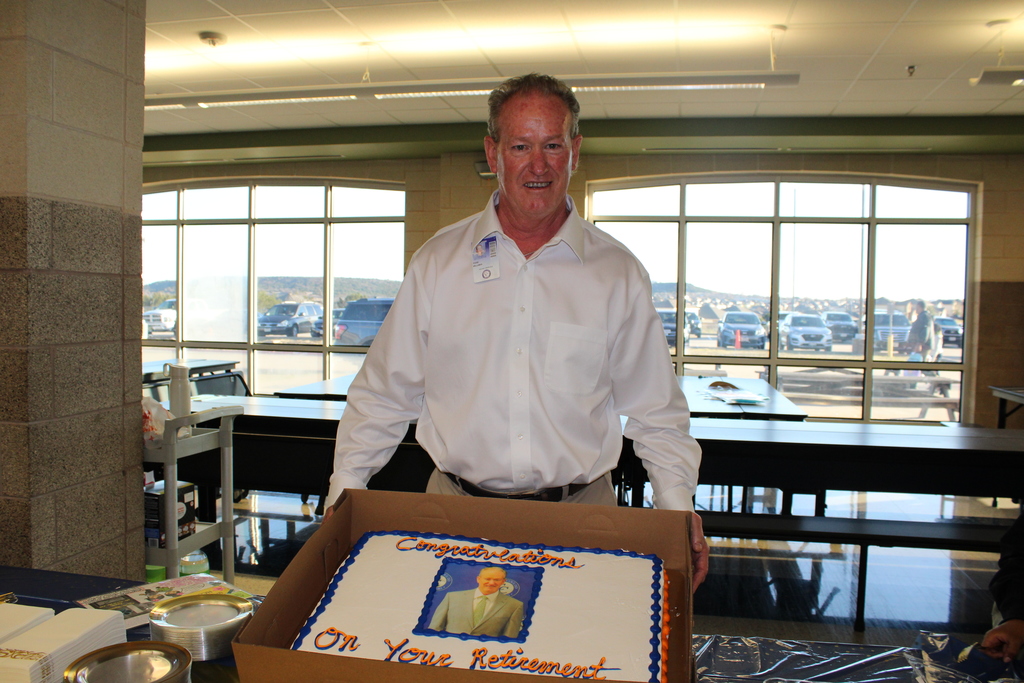 A man holding a cake in a cafeteria, smiling