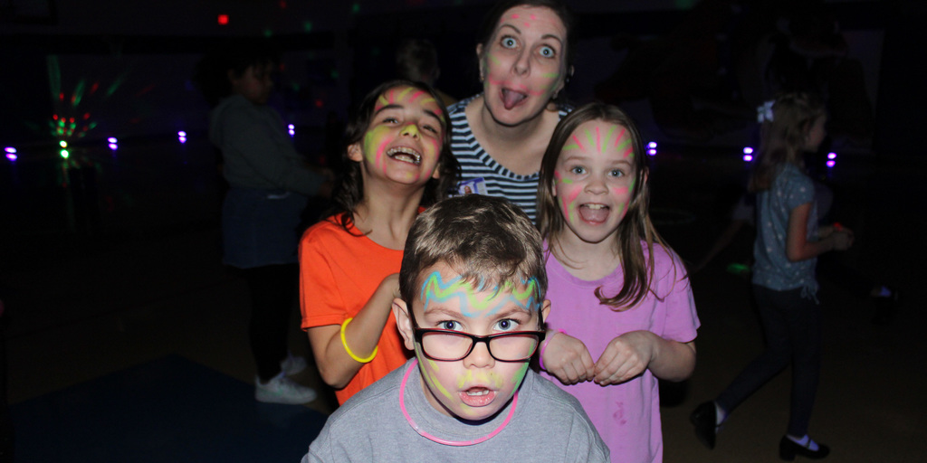 A principal and students making silly faces in a dark gym