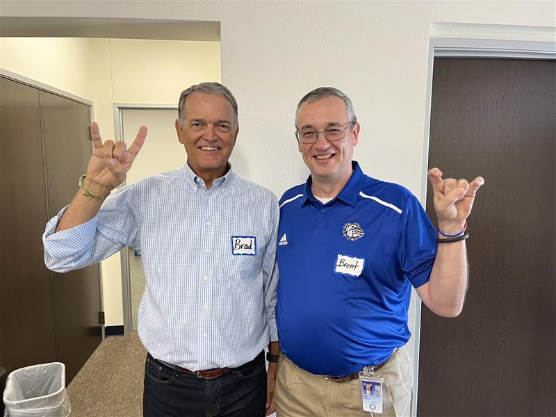 Two men holding up hand signs and smiling