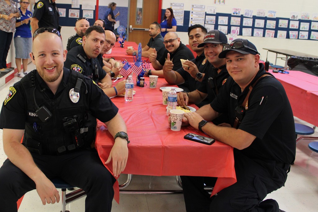 Firefighters and police sit and smile at cafeteria table