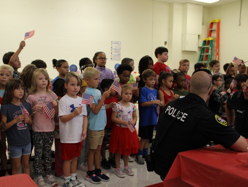 First graders line up on stage with flags to greet First Responders