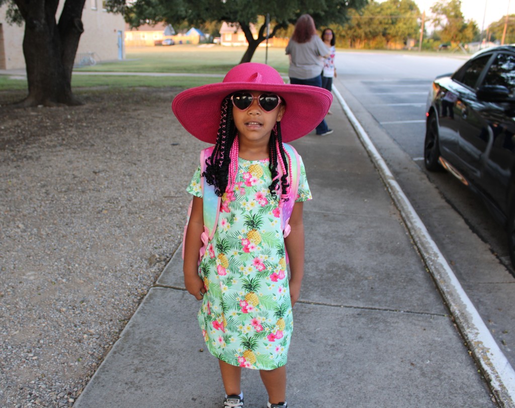 Student in pink sunhat and tropical dress poses outside school