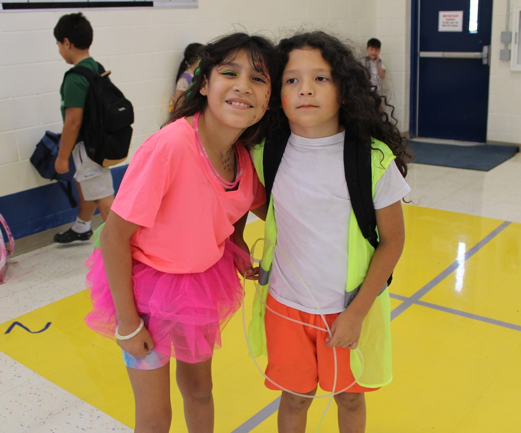 two students in neon clothes pose in gym