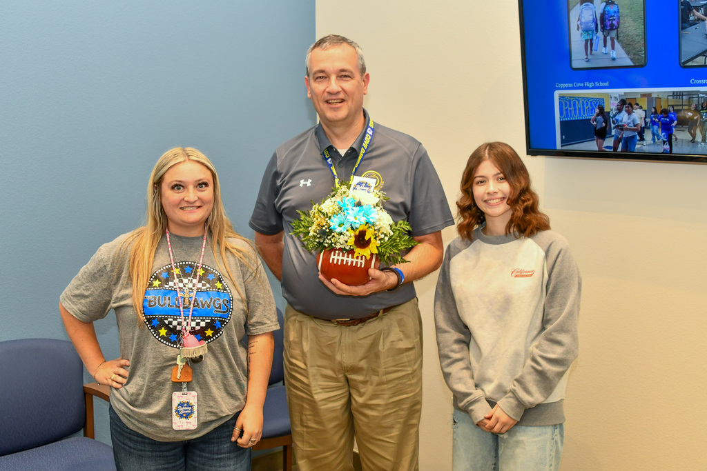 Teacher, superintendent and student smiling, holding a floral piece