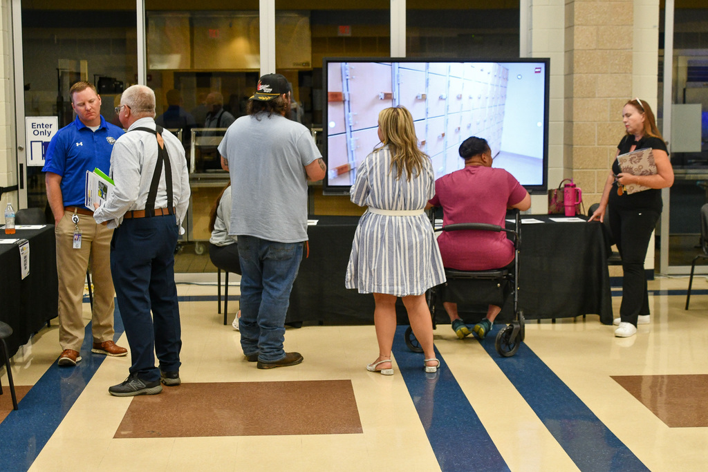 A group of people speaking with presenters in front of screens