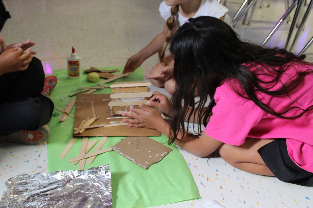 Students glue popsicle sticks to cardboard roof