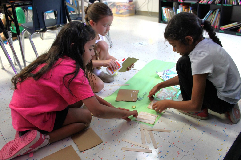 3 students glue popsicle sticks together