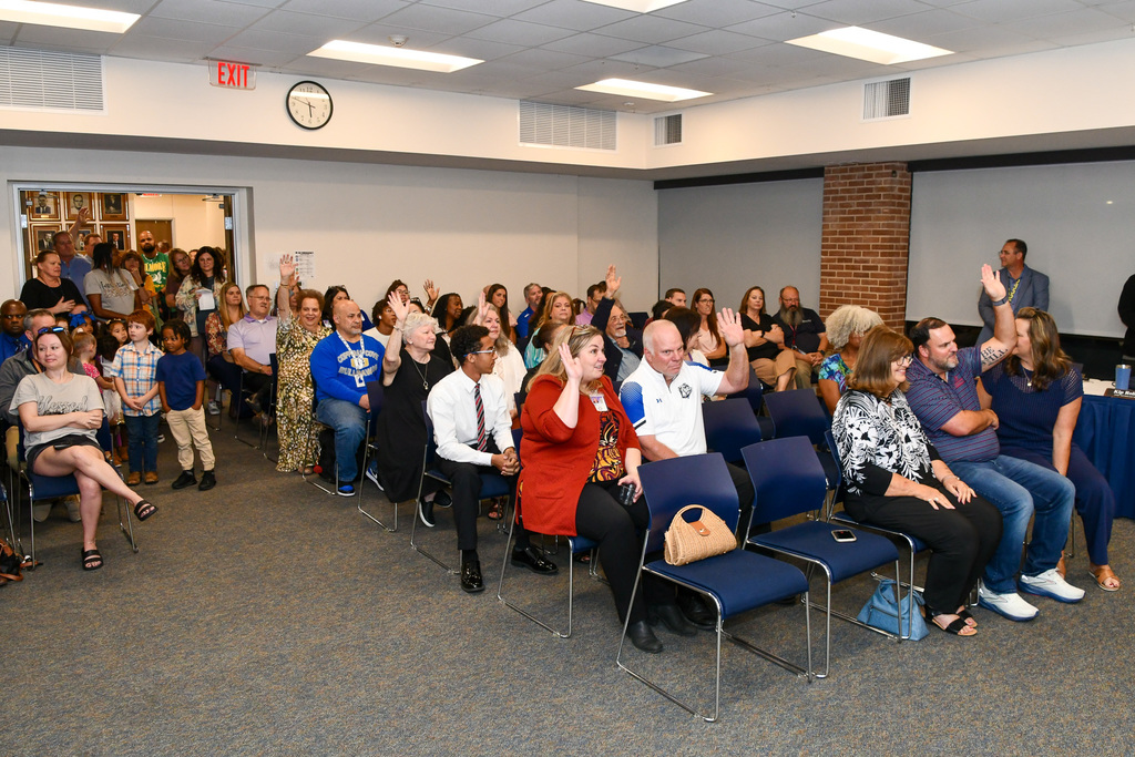 An audience sitting, several people raising their hands