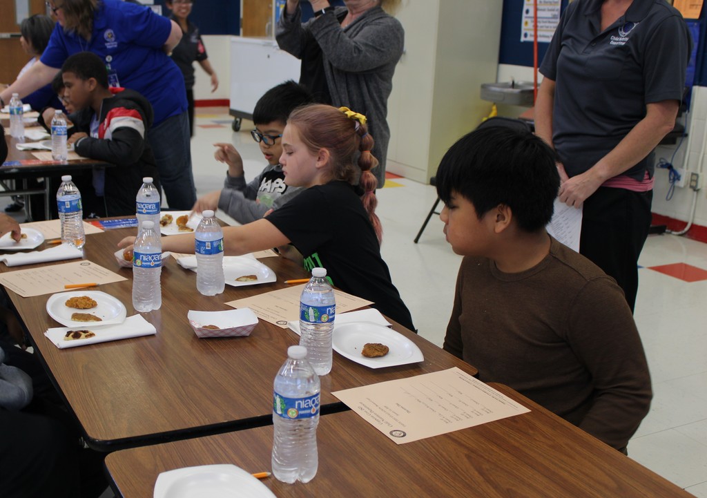 Students try food at table with rating sheet