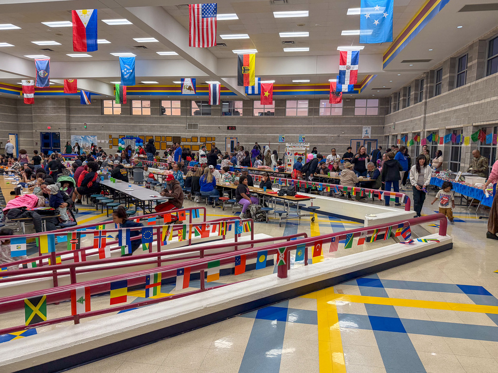 Photo of a cafeteria with people at tables and flags hanigng from the ceiling