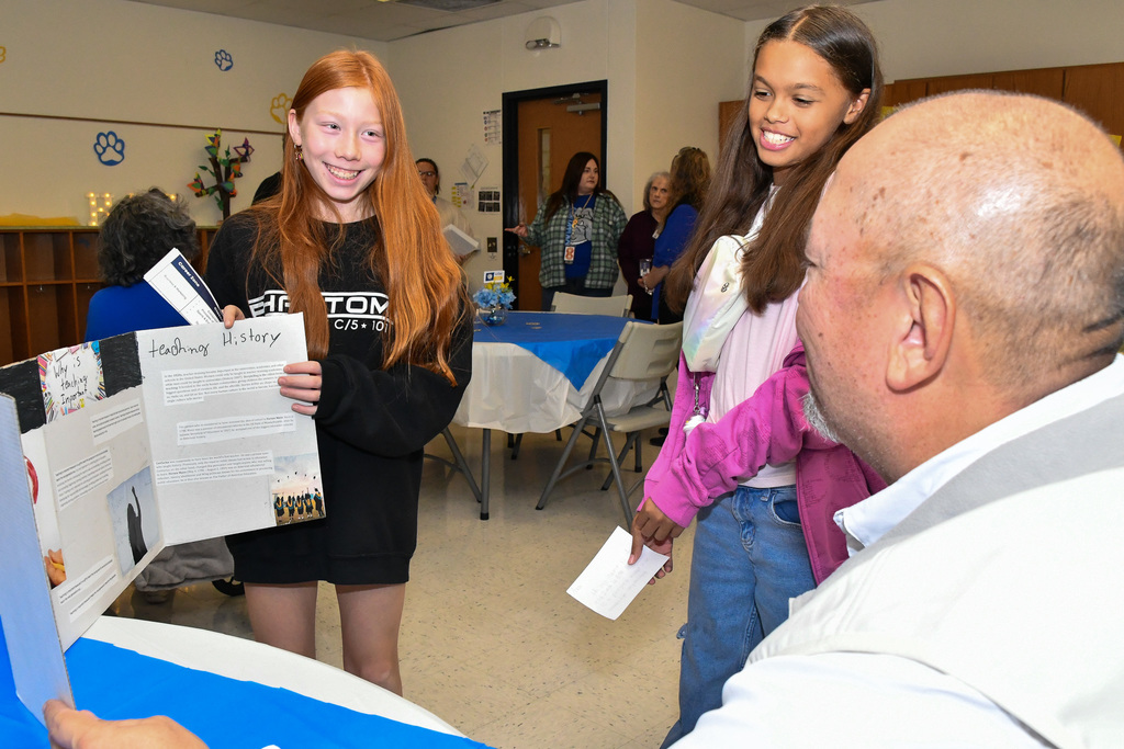 Two students smiling, presenting to an adult