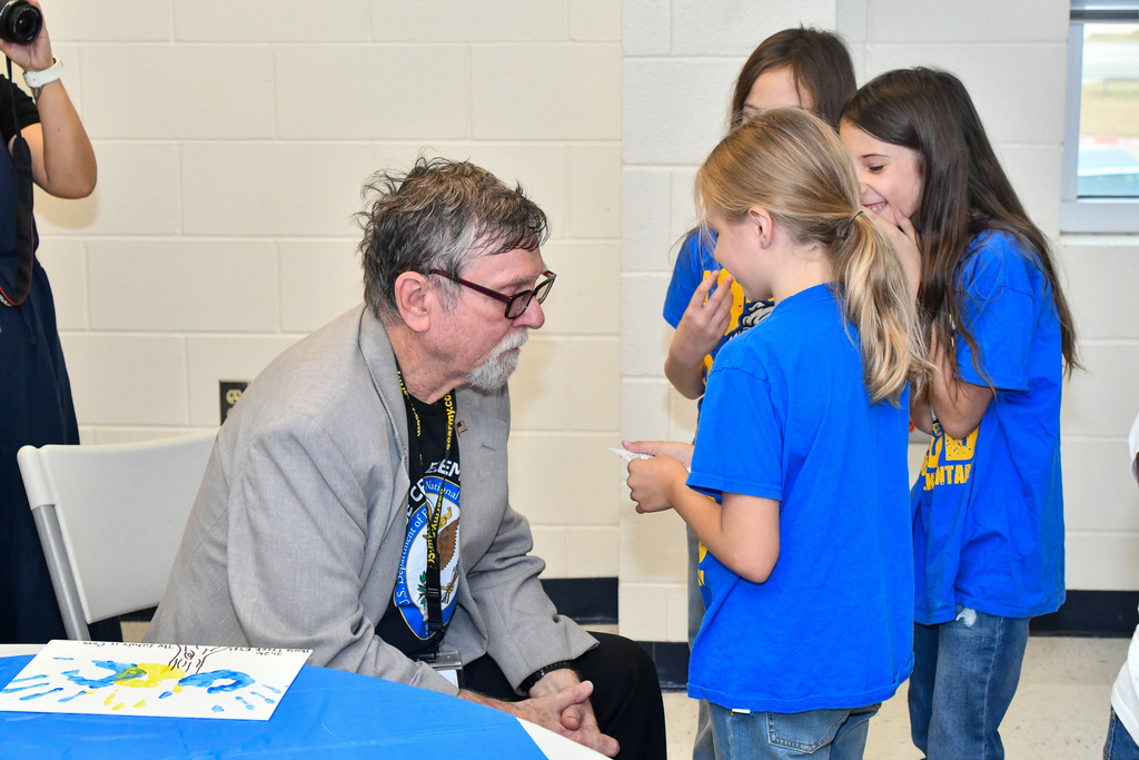 Three students smiling, presenting to a trustee