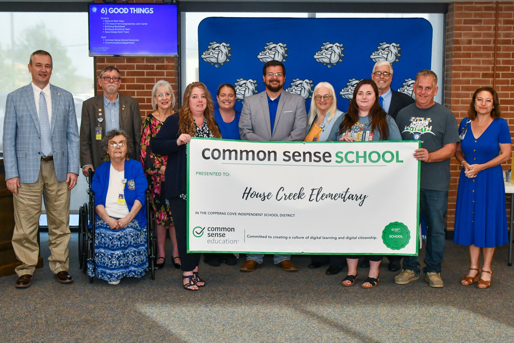 A group of teachers and trustees holding a banner and smiling in front of a backdrop