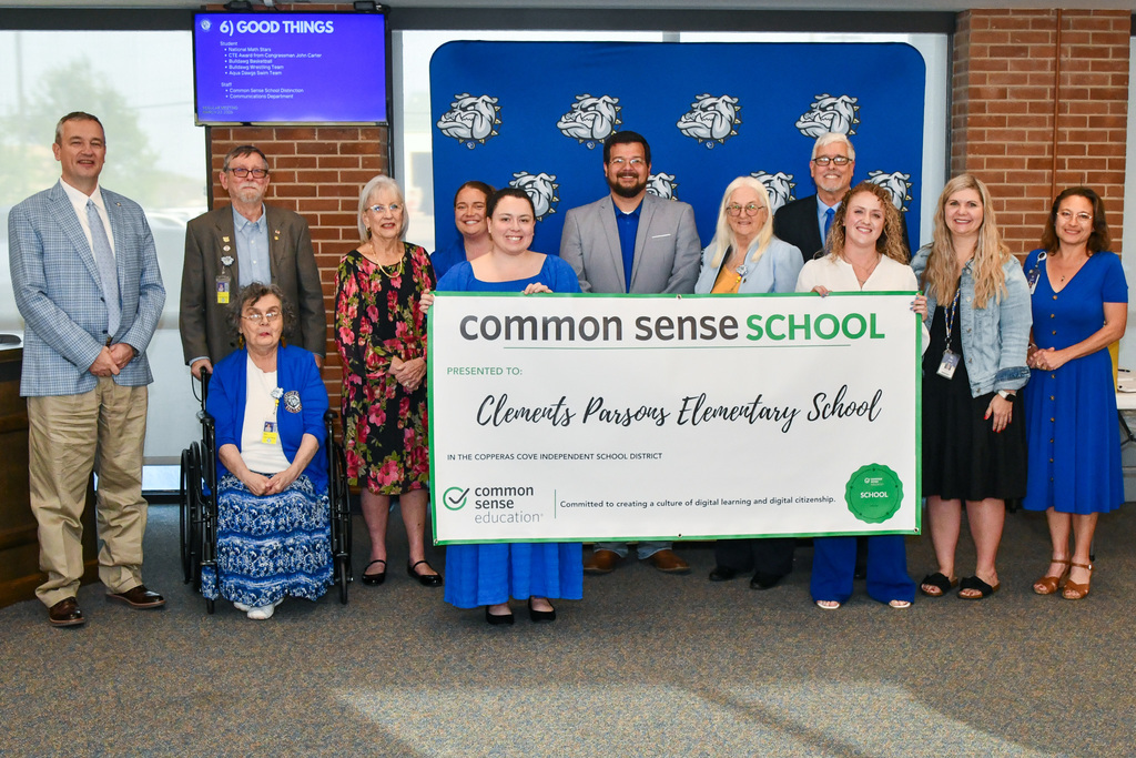 A group of teachers and trustees holding a banner and smiling in front of a backdrop