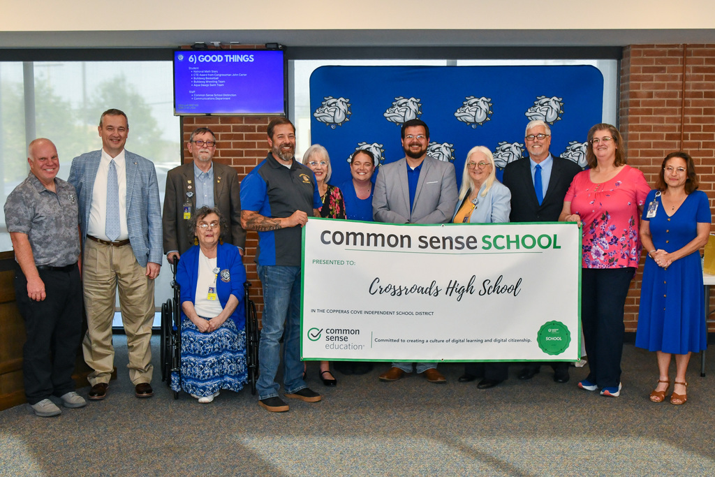 A group of teachers and trustees holding a banner and smiling in front of a backdrop